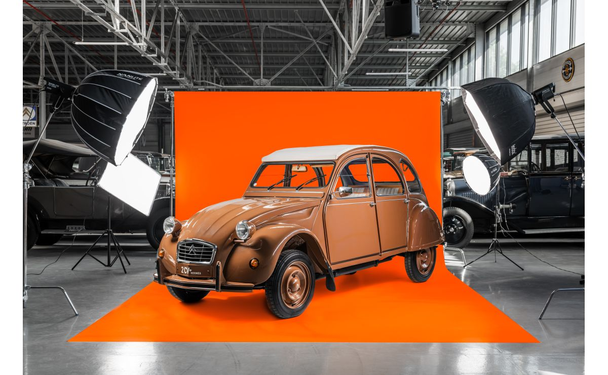 A brown Citroën 2CV by Hermès in profile against an orange studio backdrop.